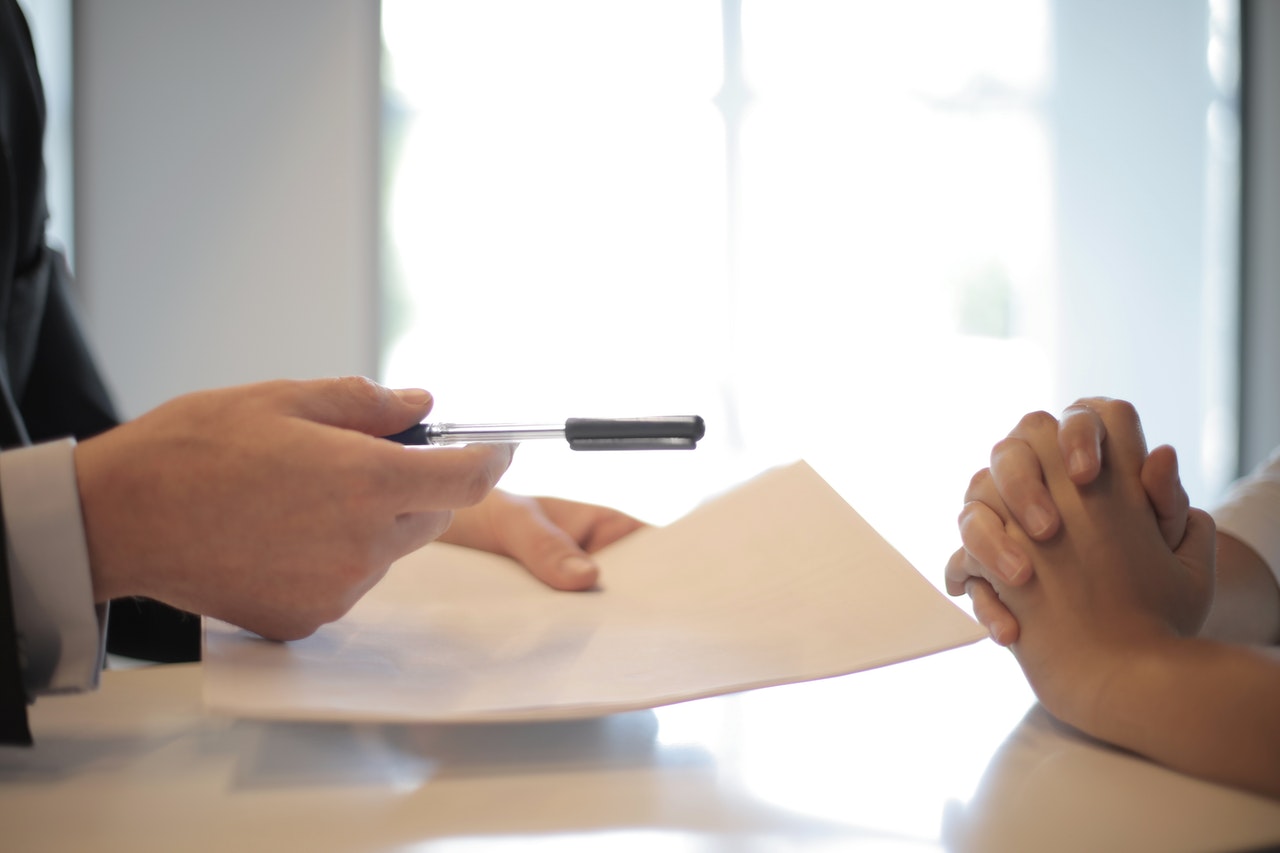 personne qui tient des documents dans une main et qui tend un stylo à une autre personne